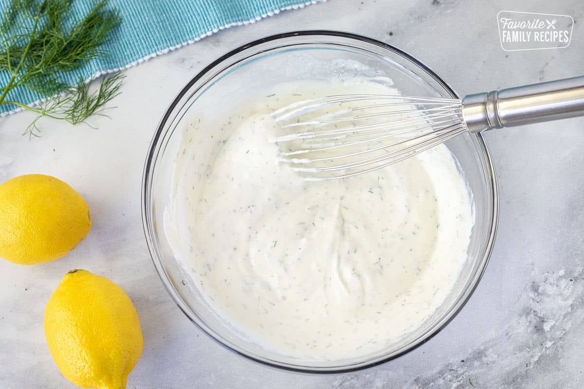 Glass bowl of Tzatziki sauce for Baked Lemon Salmon with a whisk.