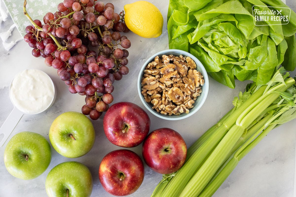 Ingredients to make Waldorf Salad including grapes, lemon, red and green apples, lettuce, celery, walnuts and mayo.