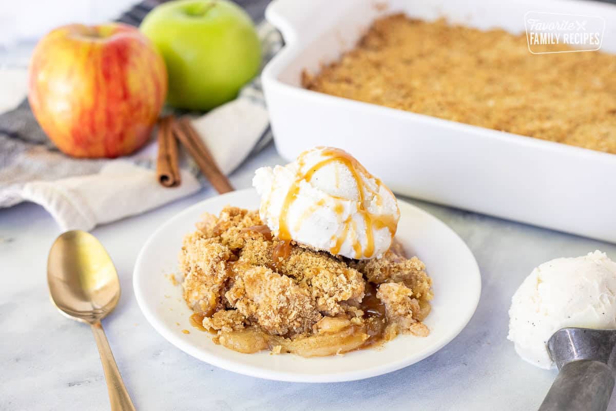 Ice cream scoop with vanilla ice cream next to a plate of Apple Crisp.