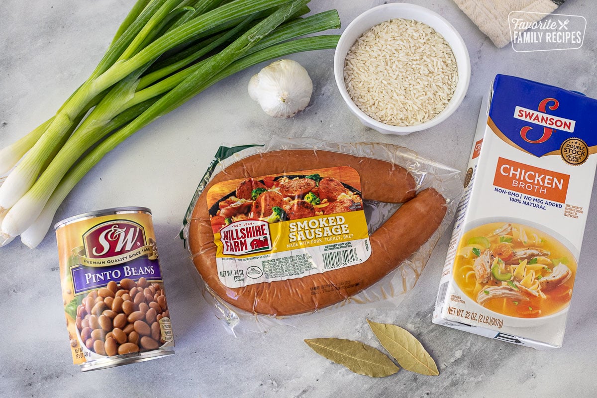 Ingredients to make Brazilian Rice and Beans including smoked sausage, rice, garlic, green onion, chicken broth, pinto beans and bay leaves.