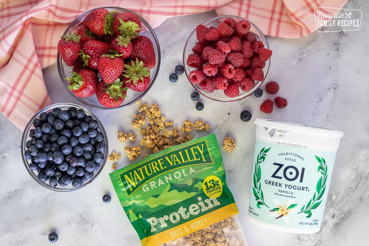 Ingredients to make Breakfast Parfaits including granola, yogurt, blueberries, strawberries and raspberries.