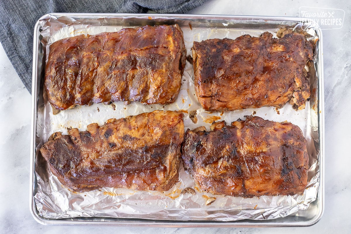 Baking sheet covered in foil with four sections of broiled baby back ribs.