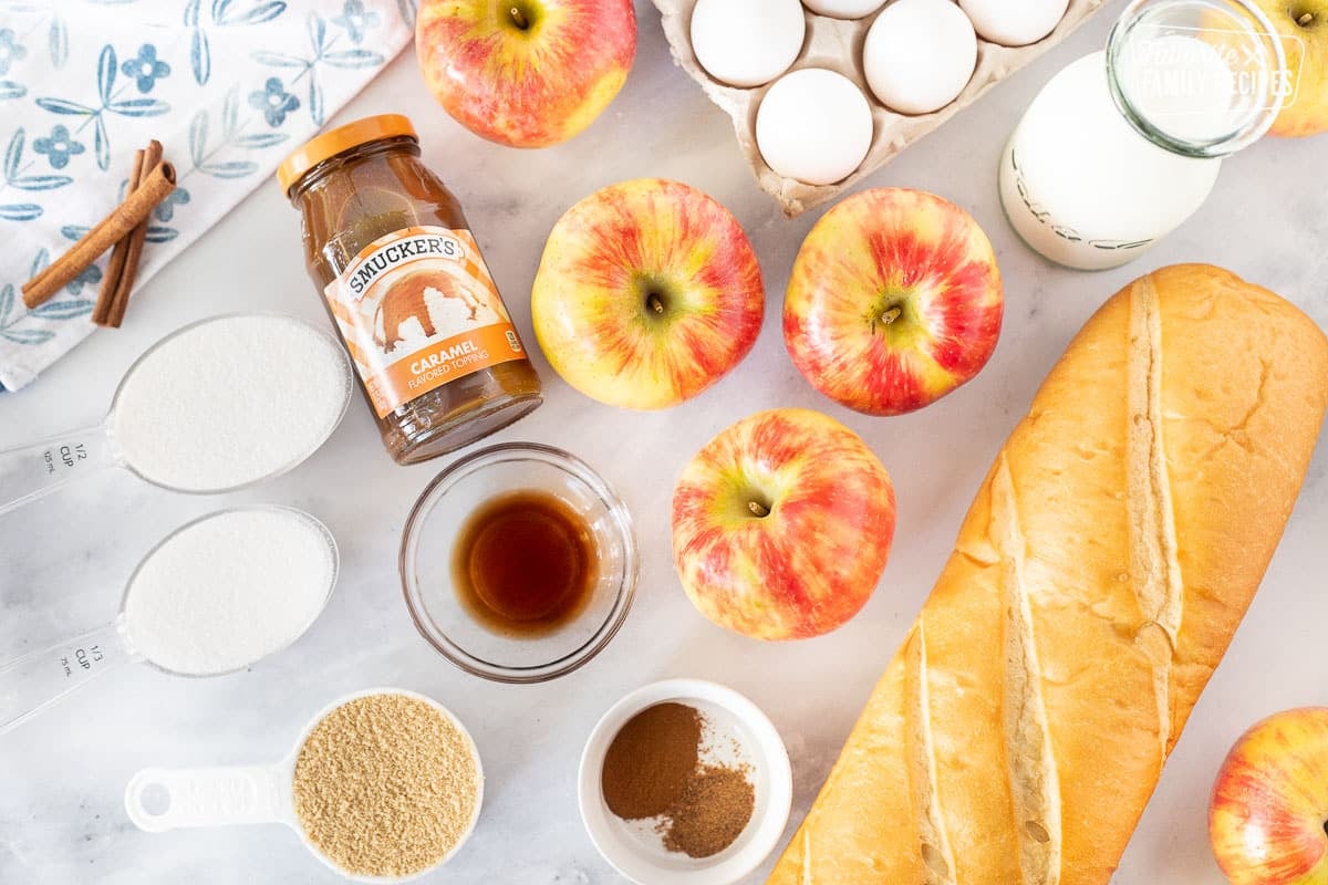 Ingredients for Caramel Apple French Toast Casserole including milk, eggs, apples, caramel, cinnamon, nutmeg, vanilla, sugars and French bread.