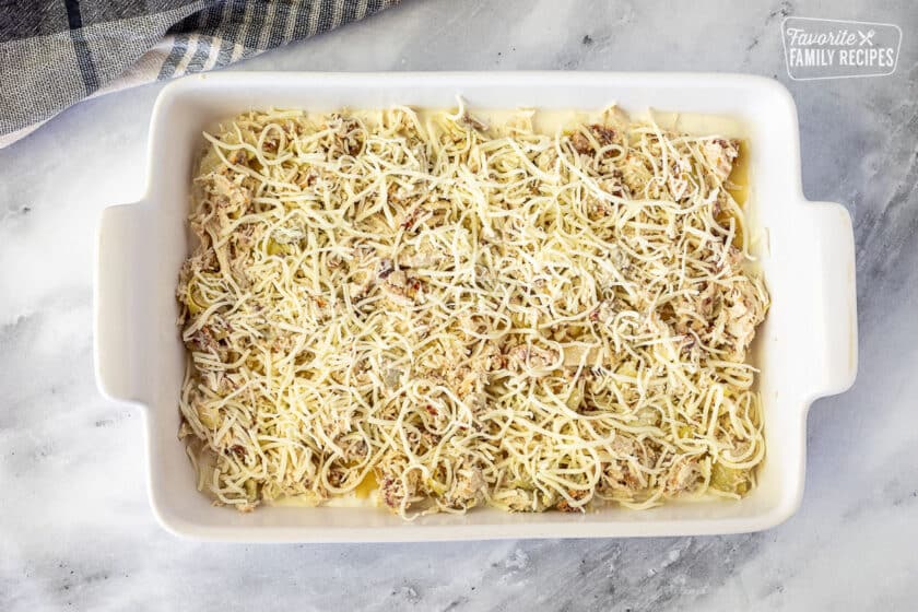 Baking dish with mozzarella cheese on top of chicken mixture layer for White Chicken Lasagna.