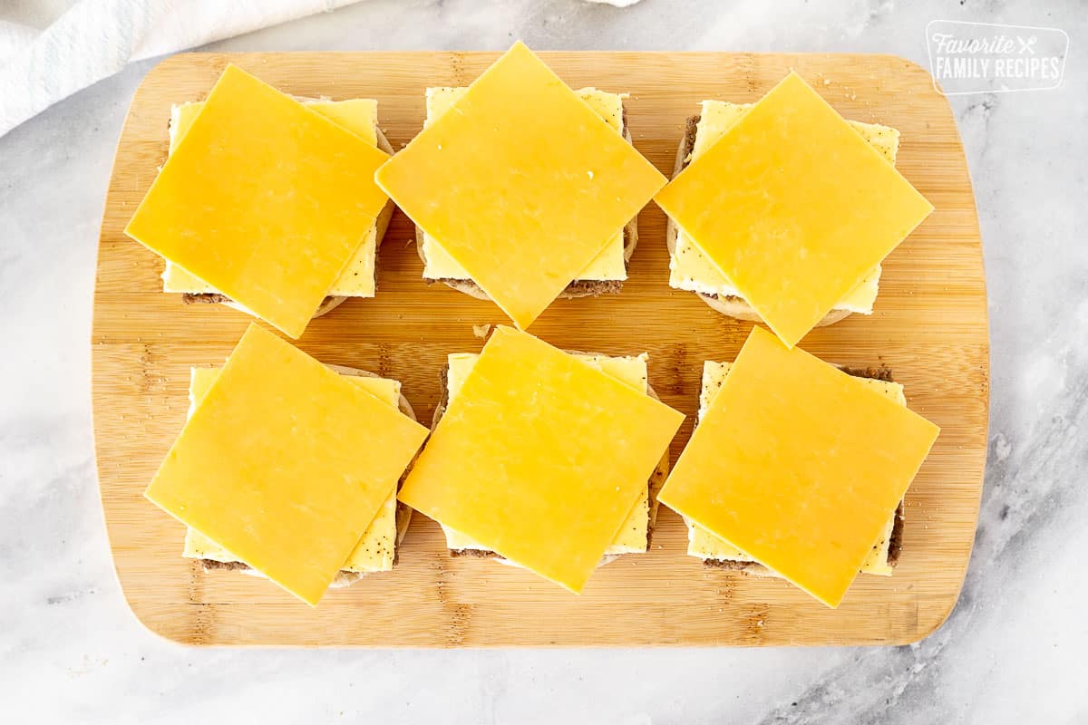 Cutting board with cheese slices on top of Freezer Breakfast Sandwiches.