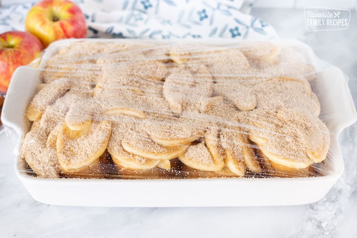 Baking dish of unbaked Caramel Apple French Toast Casserole covered in plastic wrap.