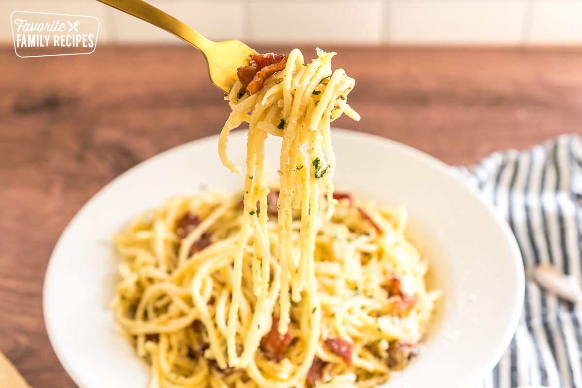 our creamy carbonara recipe in a bowl with a fork taking a bite out of it