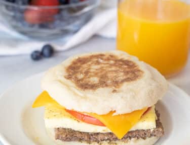 Freezer Breakfast Sandwich on a plate. Fresh berries and orange juice on the side.