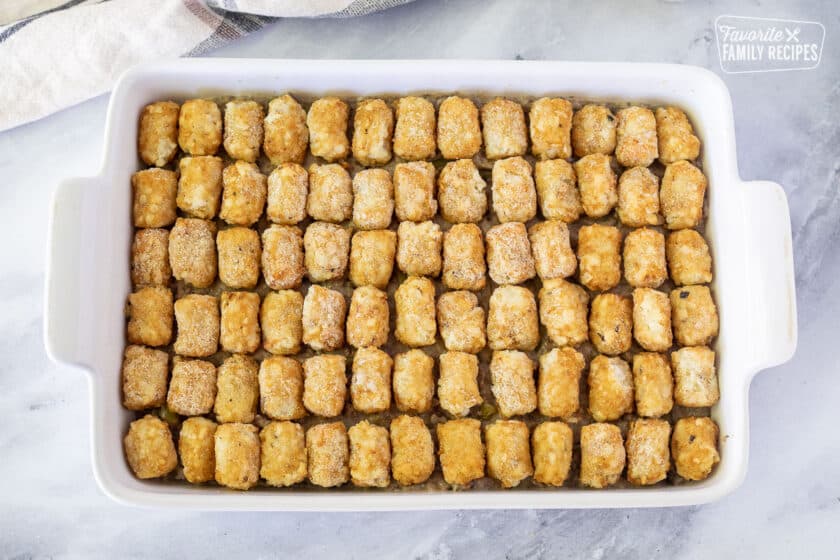 Frozen Tater Tots on top of ground beef mixture in a baking casserole dish.