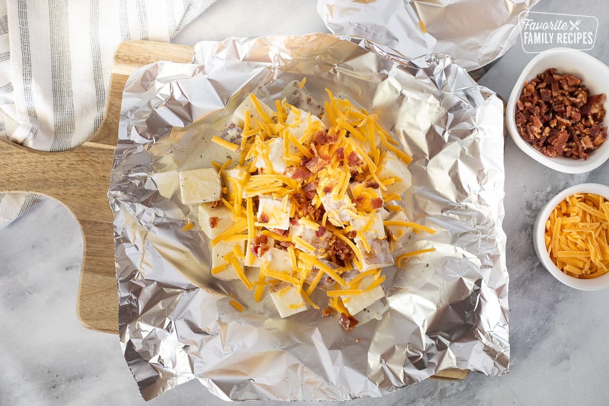 Top view of Foil with uncooked cut potatoes, cheddar cheese and bacon.