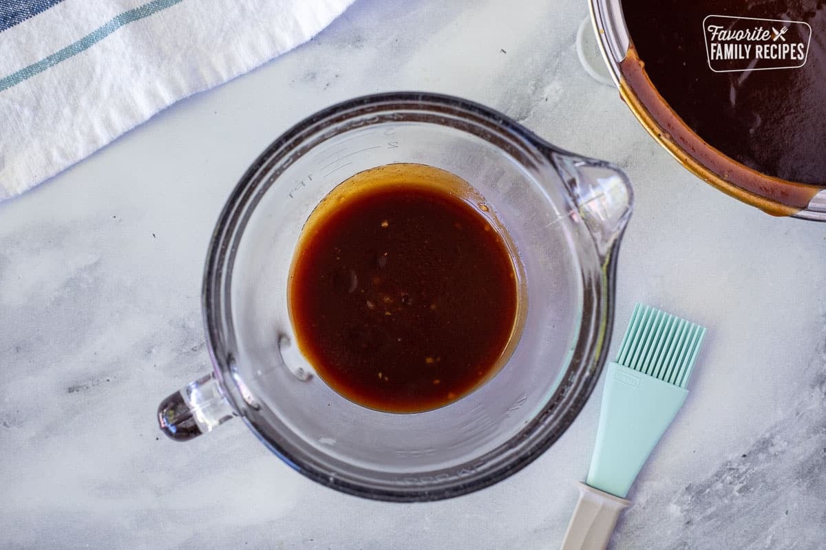 Half of the BBQ sauce in a glass bowl with brush for Honey BBQ Chicken.