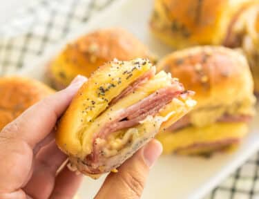 A hand holding a ham and cheese slider