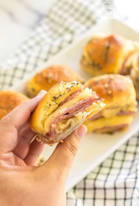 A hand holding a ham and cheese slider