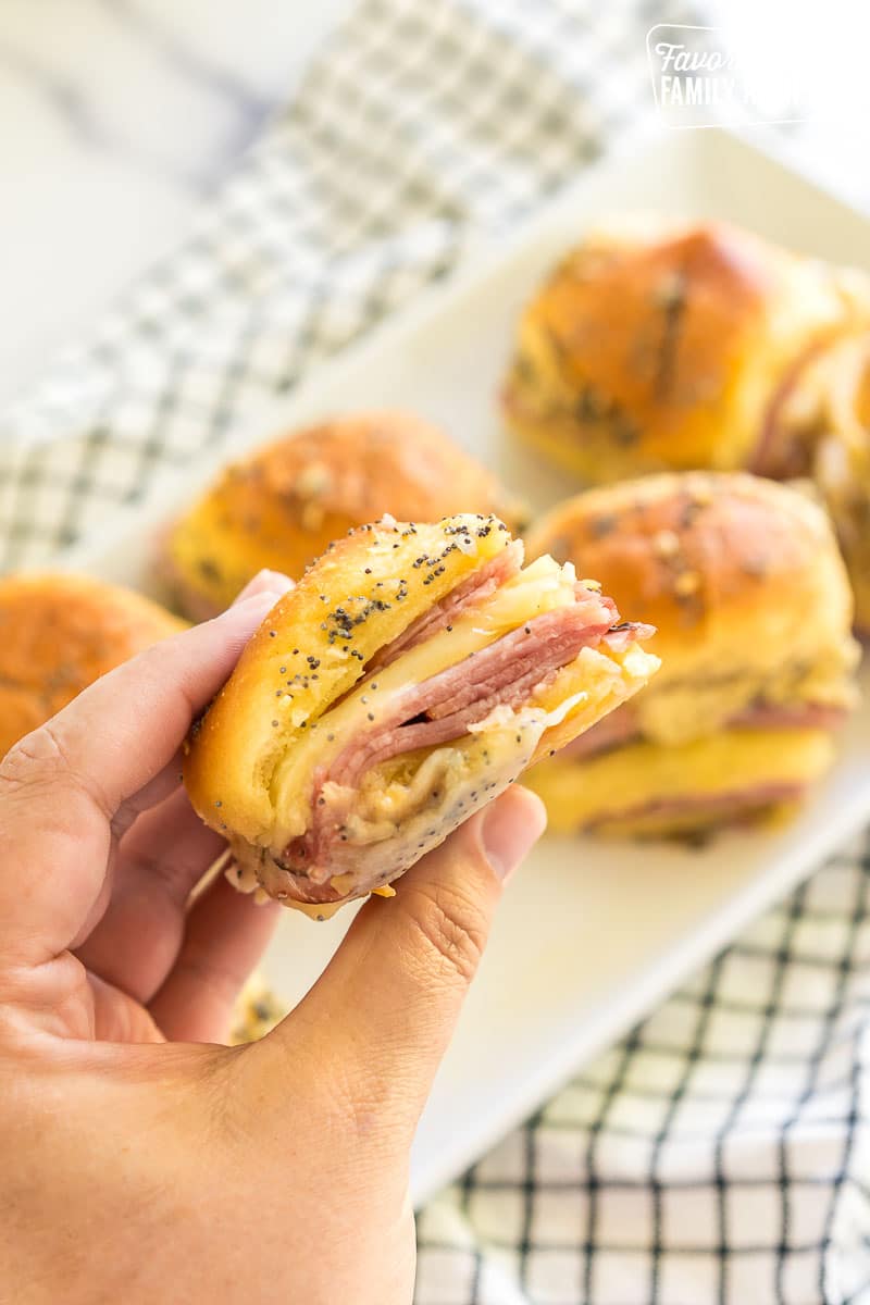 A hand holding a ham and cheese slider