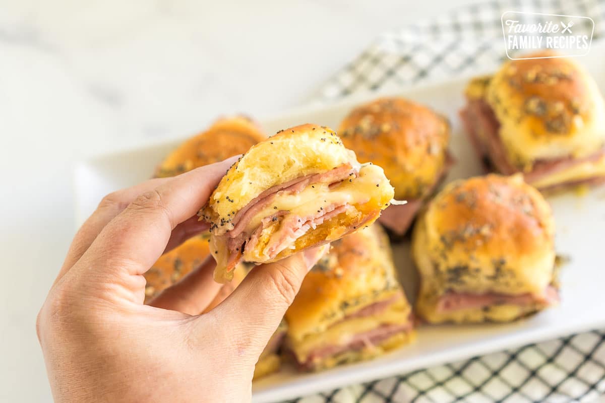 A hand holding a ham and cheese slider