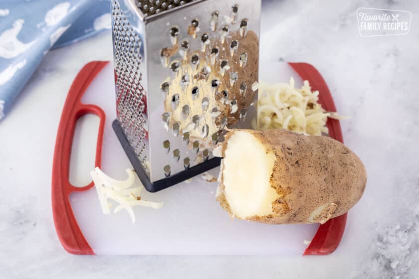 Grater and a boiled potato on a cutting board for Hash Browns.