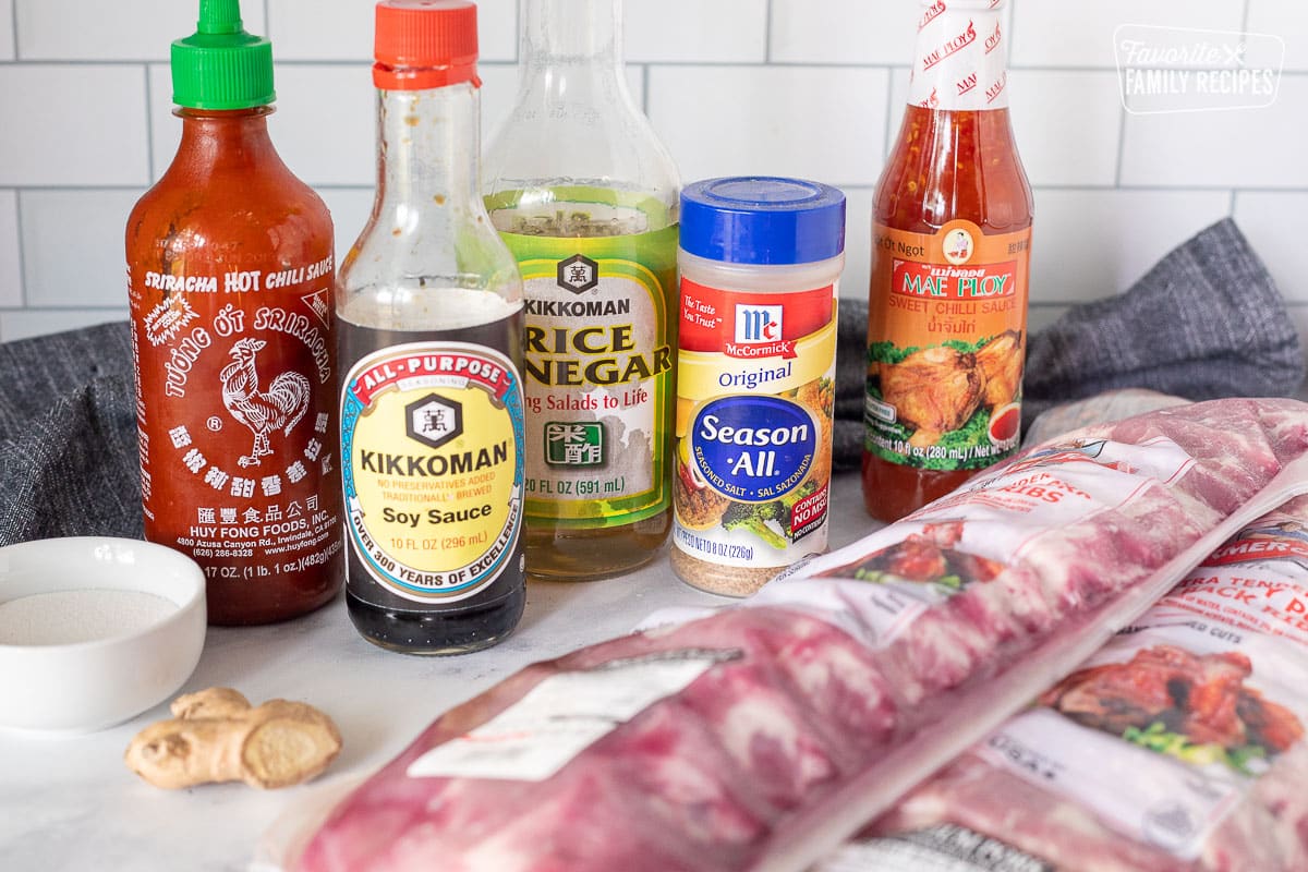 Ingredients to make Crock Pot Ribs including soy sauce, sriracha chili sauce, rice vinegar, season salt, sweet chili sauce, sugar, ginger and two racks of baby back ribs.