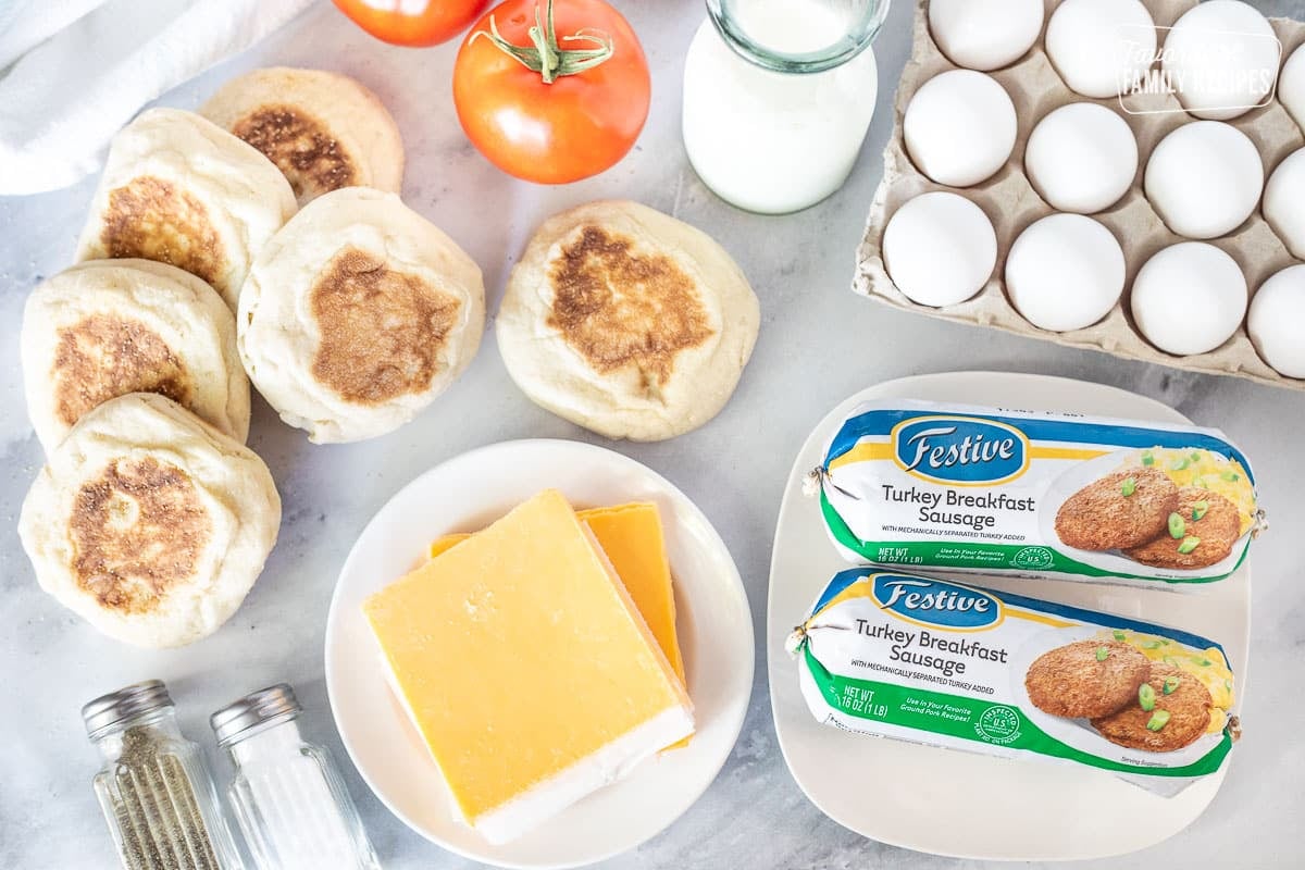 Ingredients to make Freezer Breakfast Sandwiches including English muffins, milk, eggs, turkey breakfast sausage, salt, pepper and tomato.