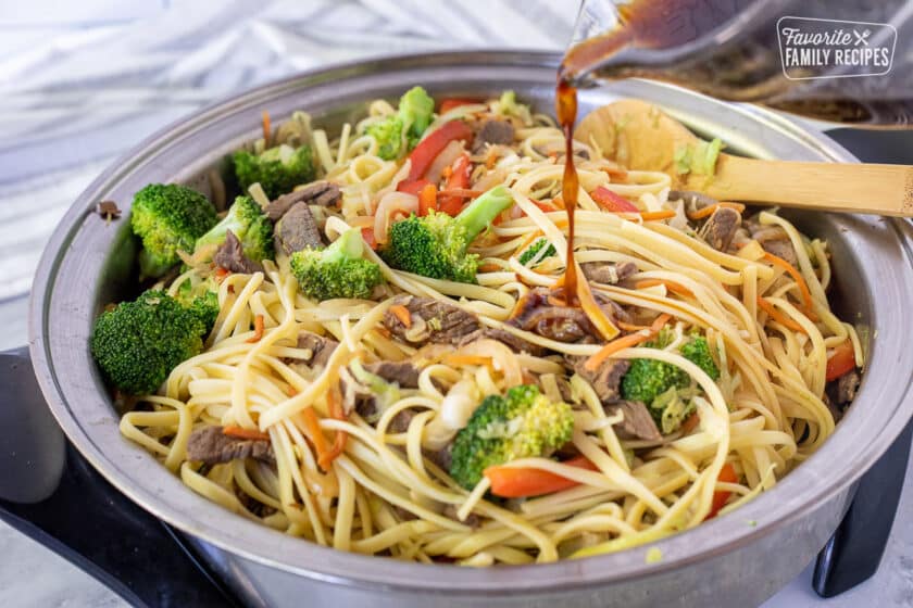 Pouring sauce into skillet of Beef Stir Fry with noodles.