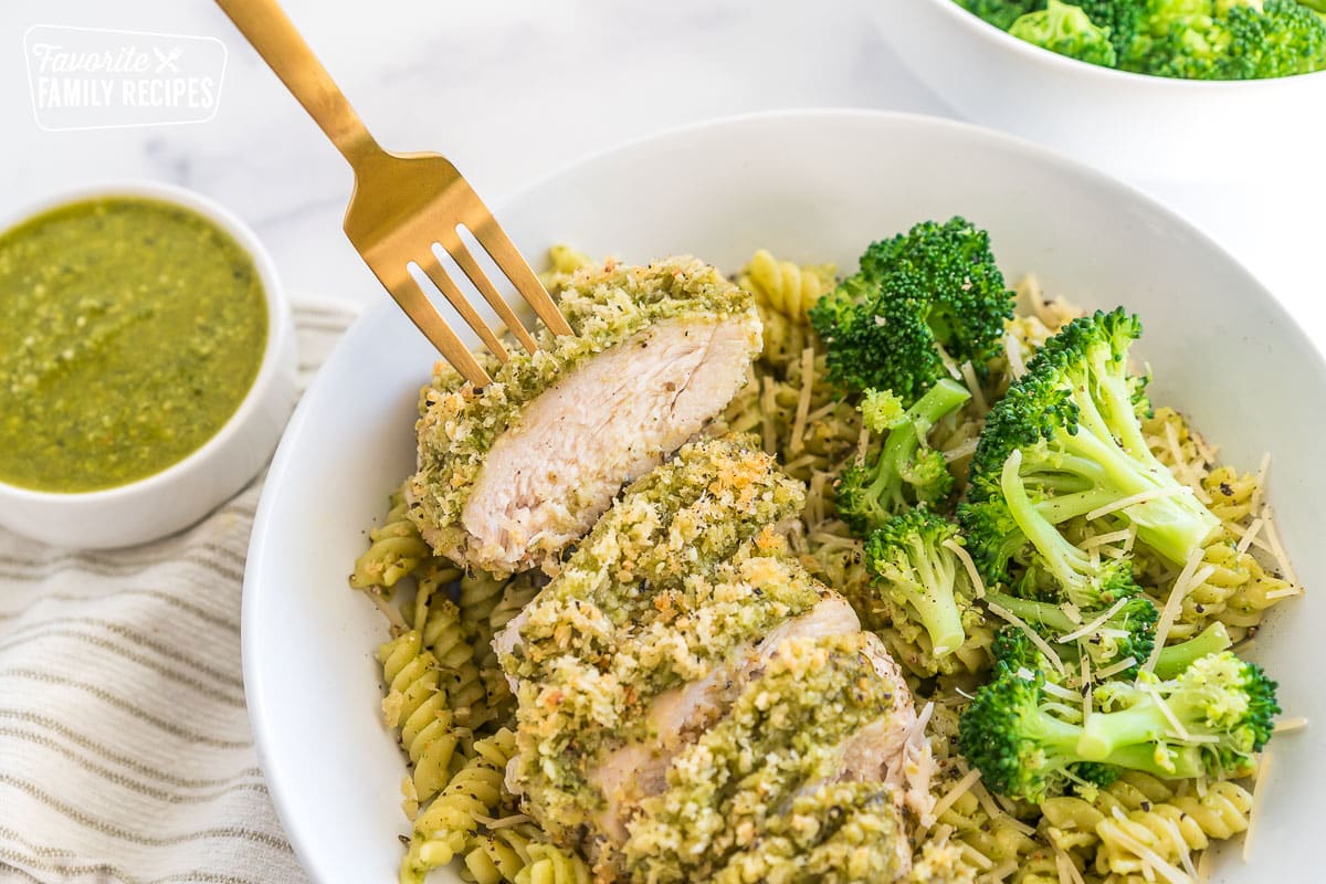a fork grabbing a piece of pesto chicken out of a bowl of pasta