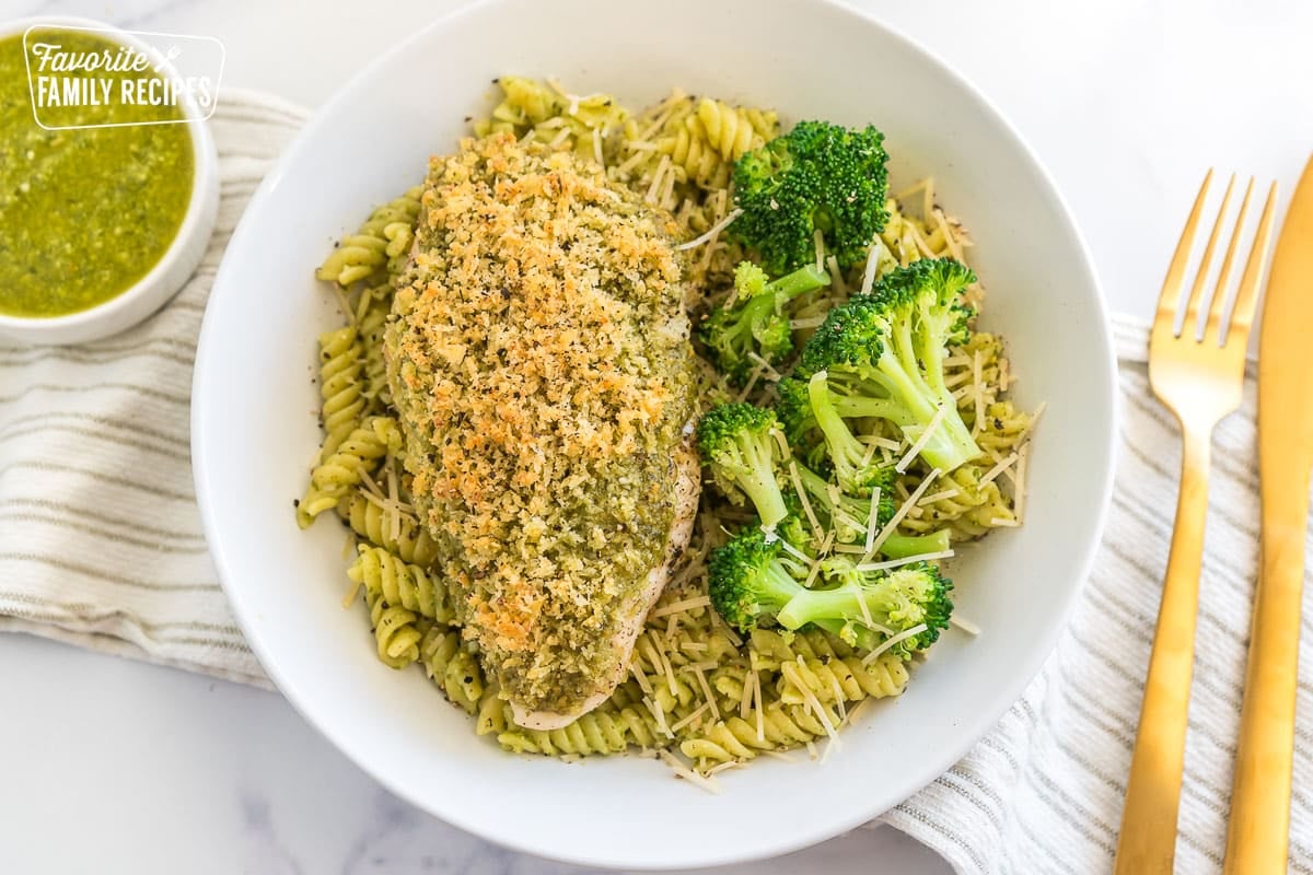 A bowl of pasta with a piece of pesto chicken on top and broccoli