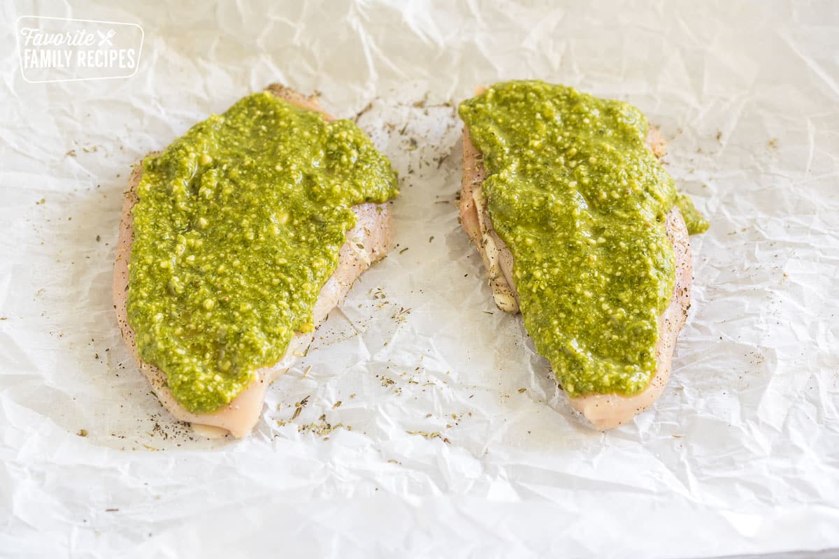 two pieces of raw chicken with pesto sauce spread on top