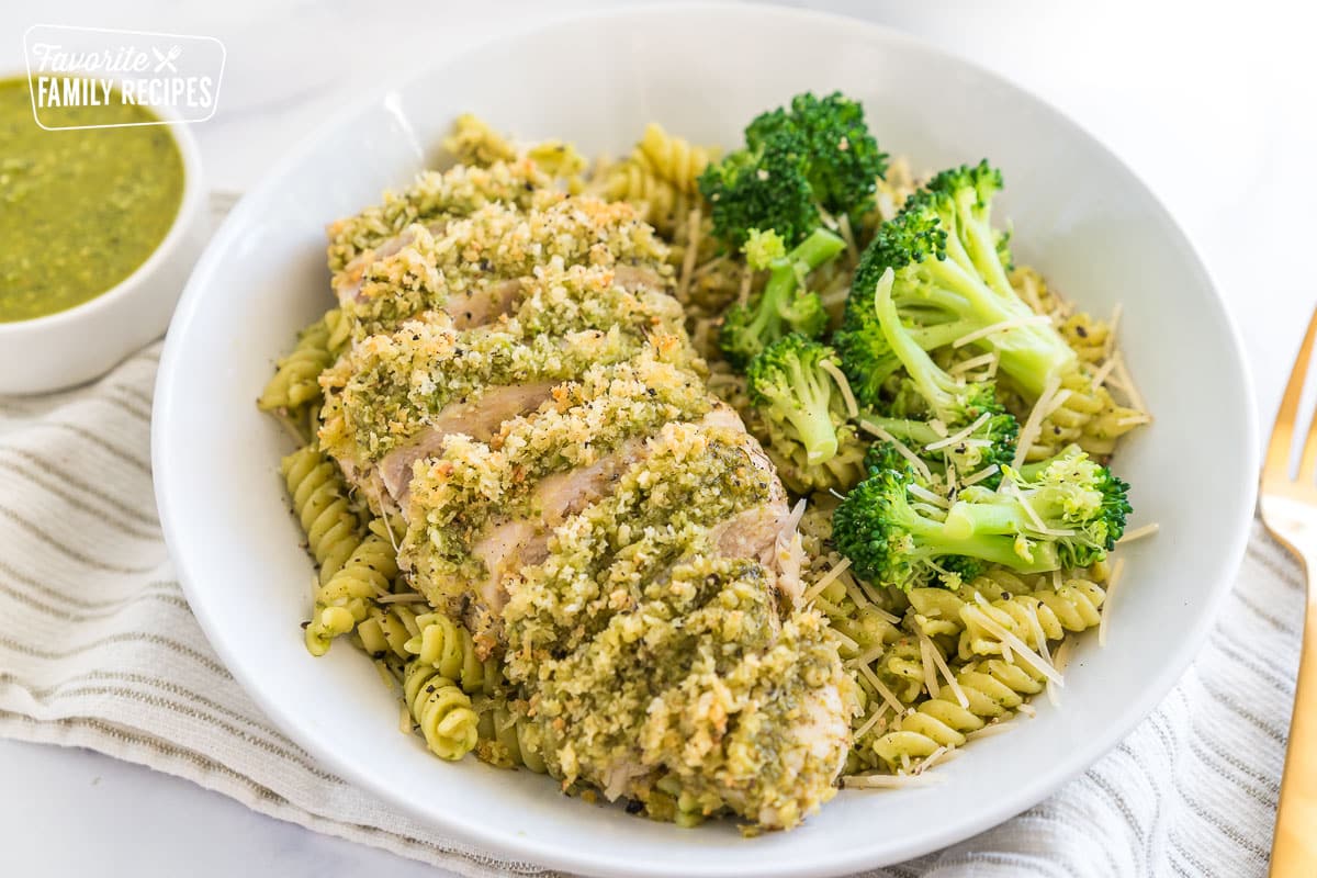 A bowl of pasta with a piece of sliced pesto chicken on top and broccoli