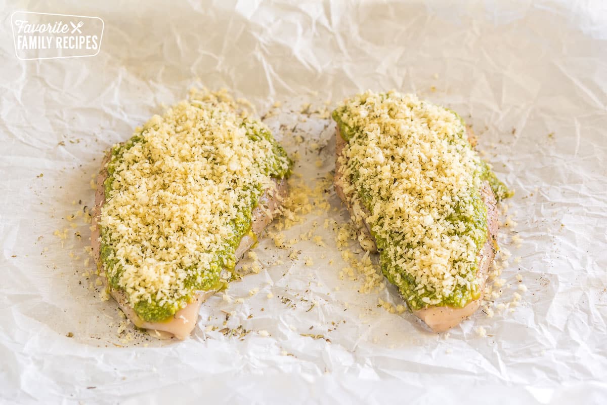 two pieces of raw chicken with pesto spread over the top and panko bread crumbs sprinkled on top