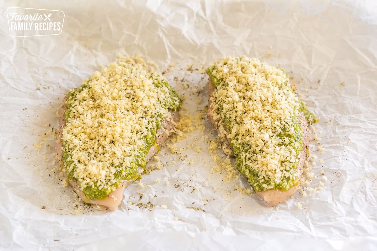 two pieces of raw chicken with pesto spread over the top and panko bread crumbs sprinkled on top