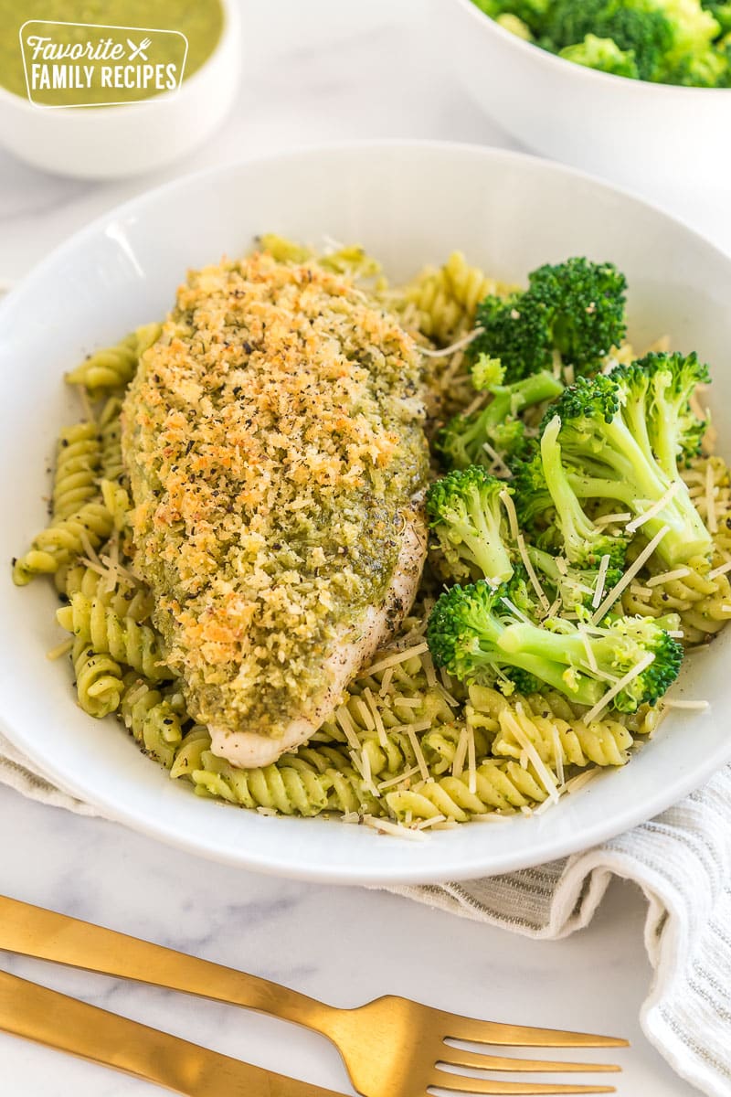 A bowl of pasta with a piece of pesto chicken on top and broccoli