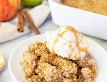 Plate with a piece of Apple Crisp topped with vanilla ice cream and caramel.