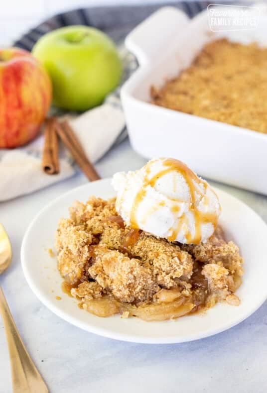 Plate with a piece of Apple Crisp topped with vanilla ice cream and caramel.