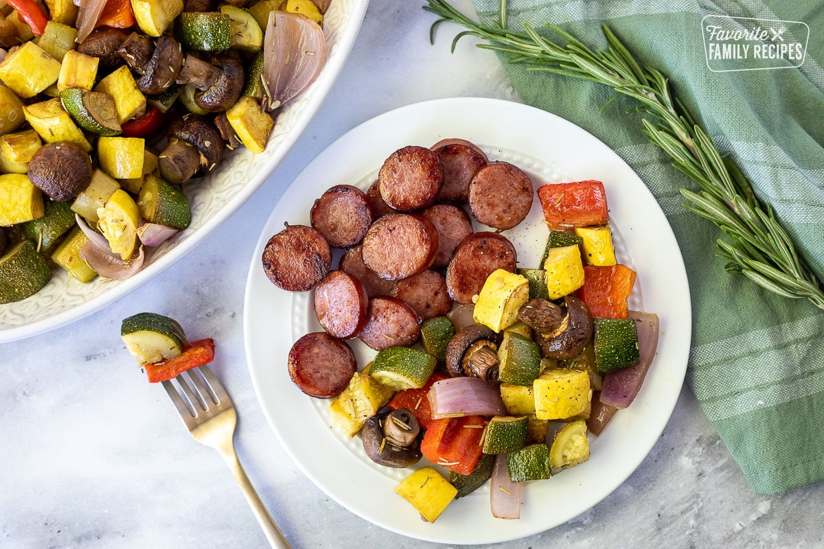 Fork with Oven Roasted Vegetables next to the plate with vegetables and kielbasa sausage.