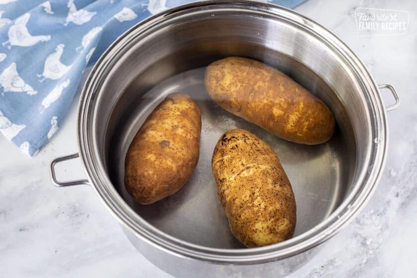 Three potatoes in a pot of water to make Hash Browns.