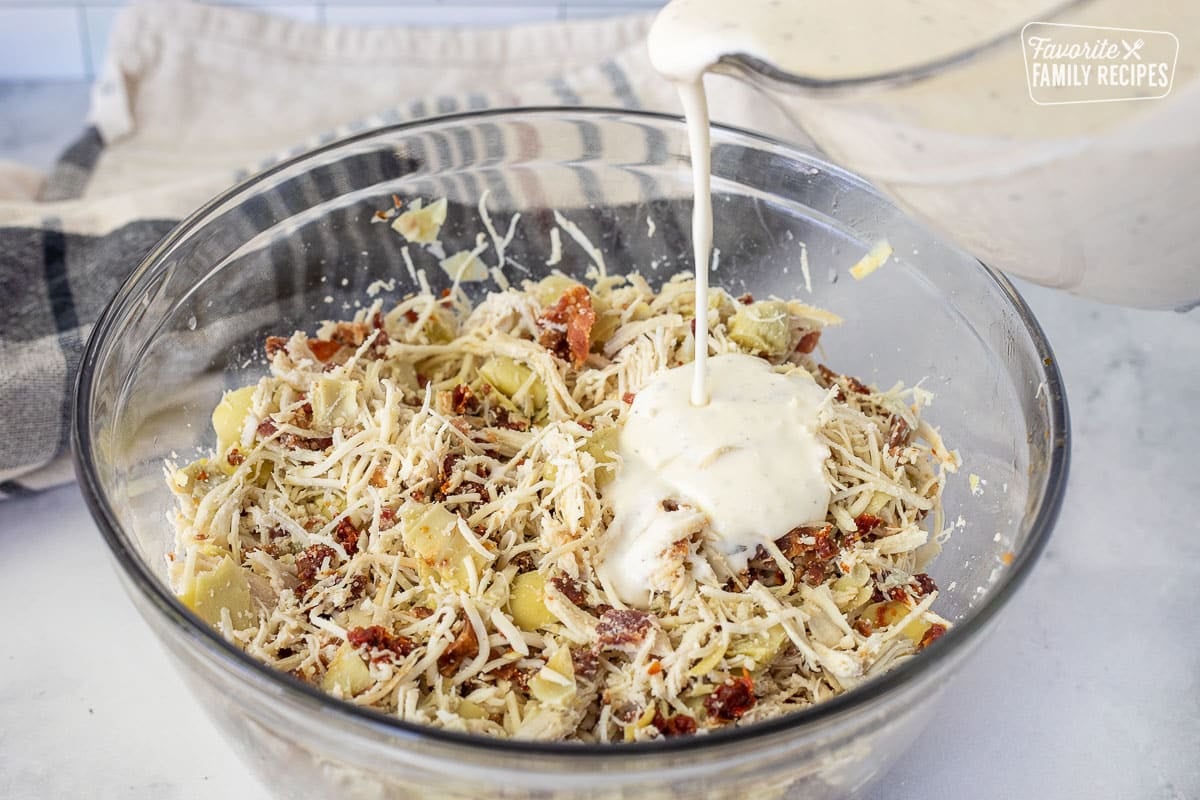 Pouring Ranch sauce into a bowl with White Chicken Lasagna filling.