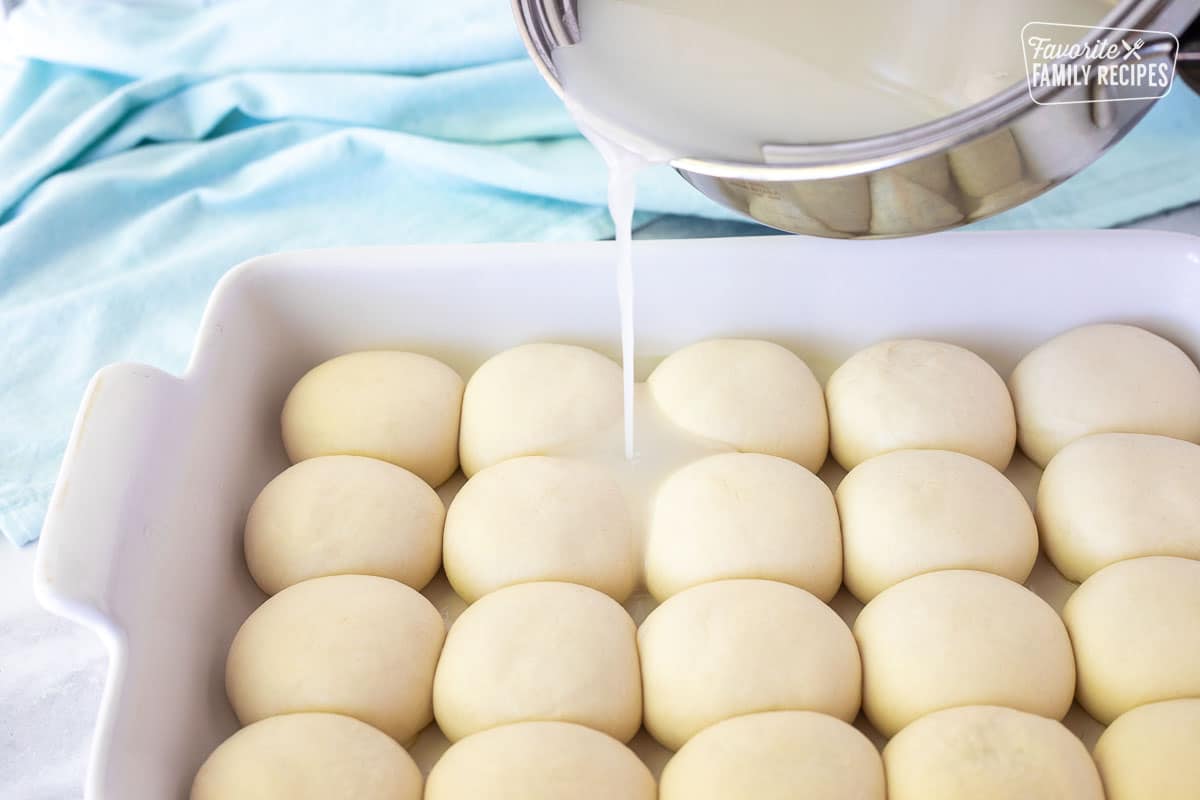 Pouring Pani Popo sauce over unbaked risen dinner rolls.