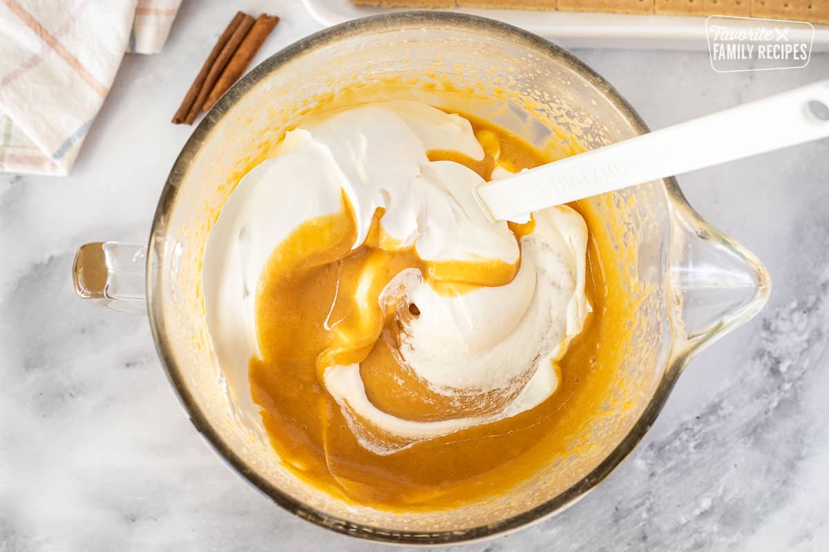 Mixing bowl with pumpkin pudding and Cool Whip for Pumpkin Eclair Cake.