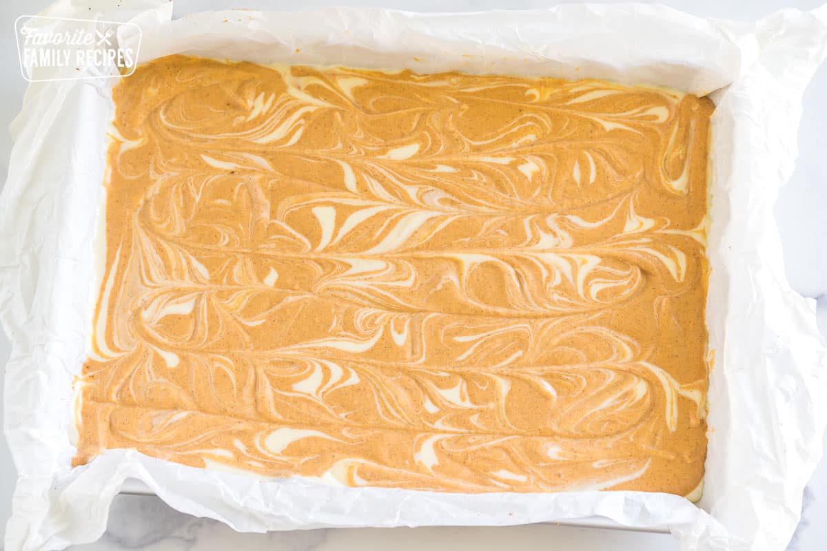 Swirled pumpkin and regular cheesecake filling on top of a graham cracker crust in a baking dish