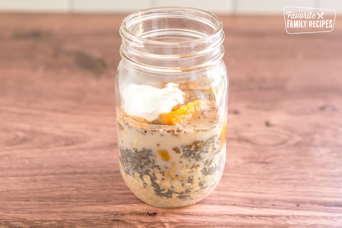A mason jar containing oats, chia seeds, pumpkin pie spice, pumpkin puree, almond milk, greek yogurt, and salt.