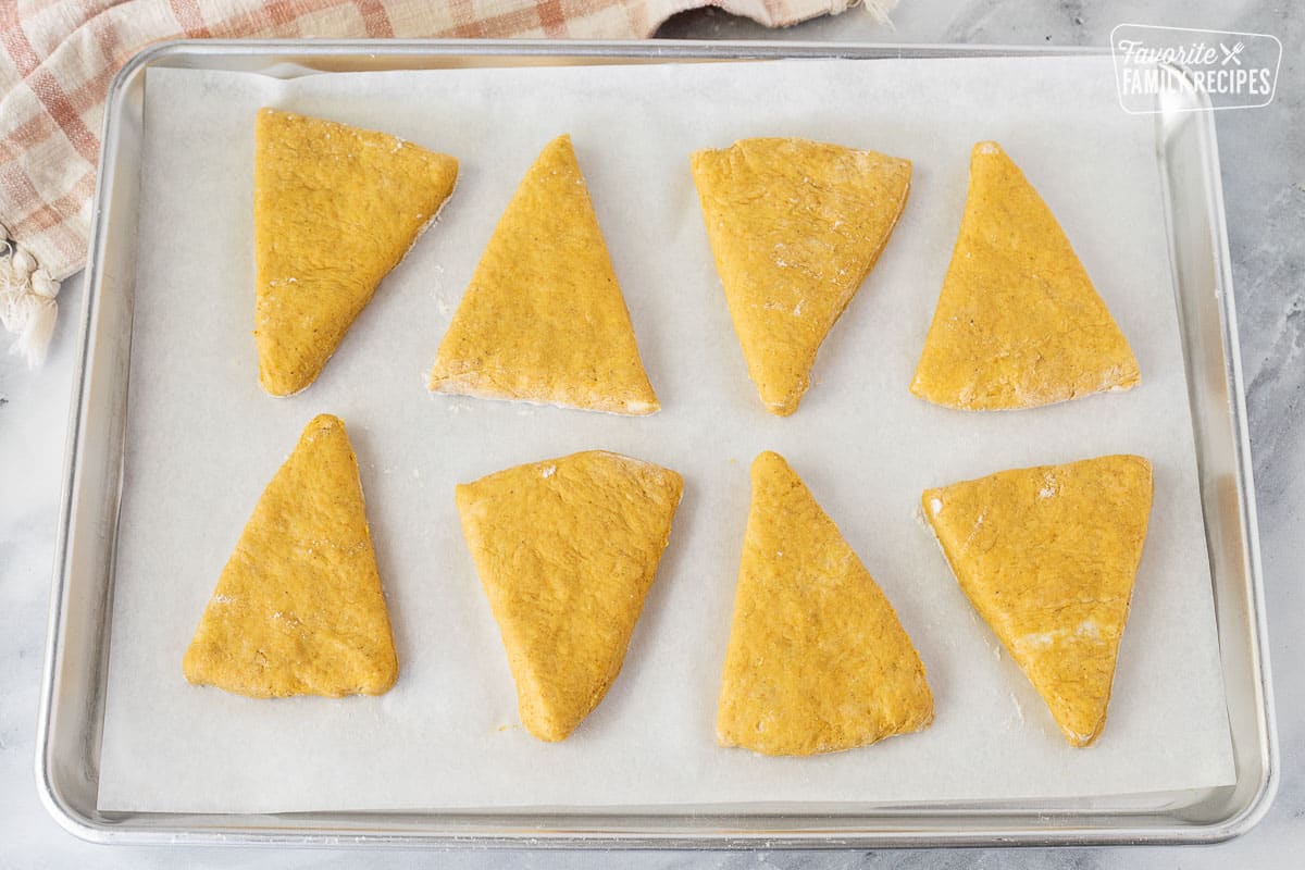 Baking sheet with parchment paper and eight unbaked Pumpkin Scone triangles.