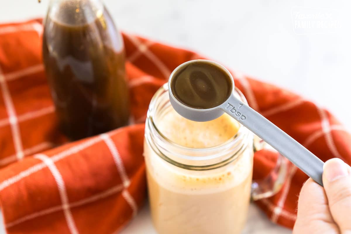 a tablespoon of pumpkin spice syrup held over a mug of coffee