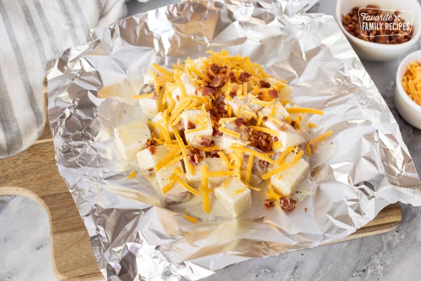 Foil with uncooked Ranch Potatoes topped with cheddar cheese and bacon.