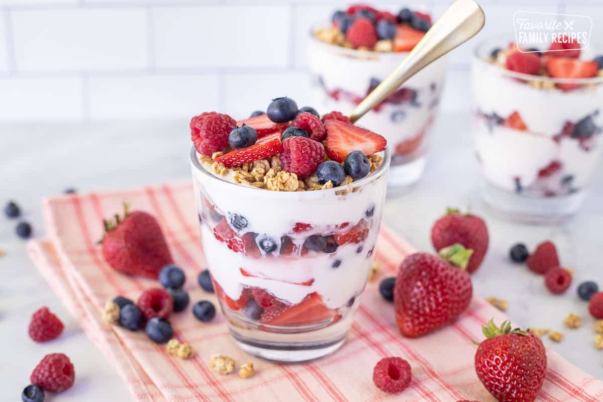 Spoon resting in a Breakfast Parfait topped with granola, raspberries, blueberries and strawberries.