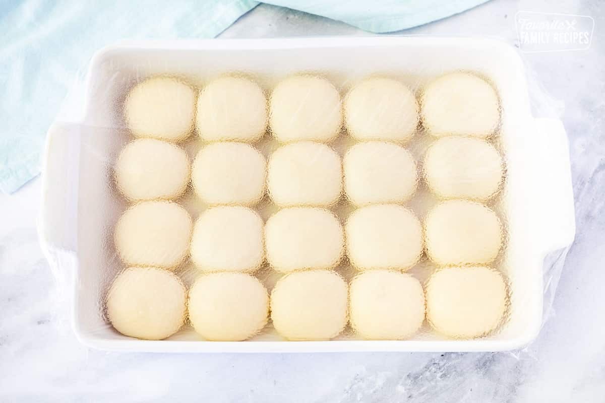 Rolls rising in greased baking dish covered with plastic wrap for Pani Popo.