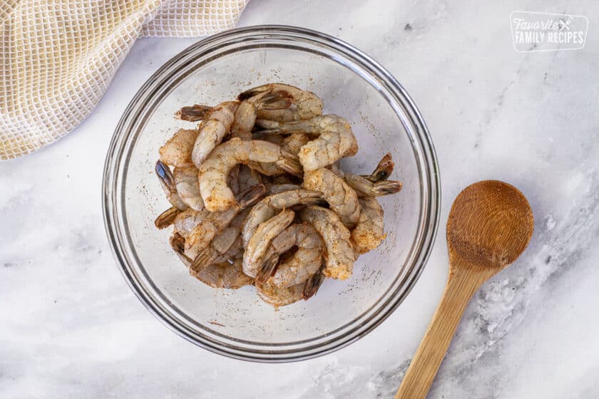 Bowl of seasoned shrimp with a wooden spoon for Creamy Cajun Shrimp Pasta.