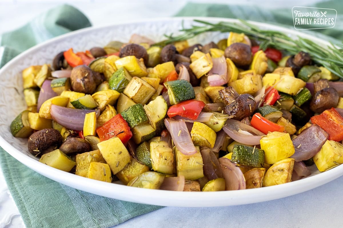 Serving tray with Oven Roasted Vegetables and garnished on the side with fresh rosemary.