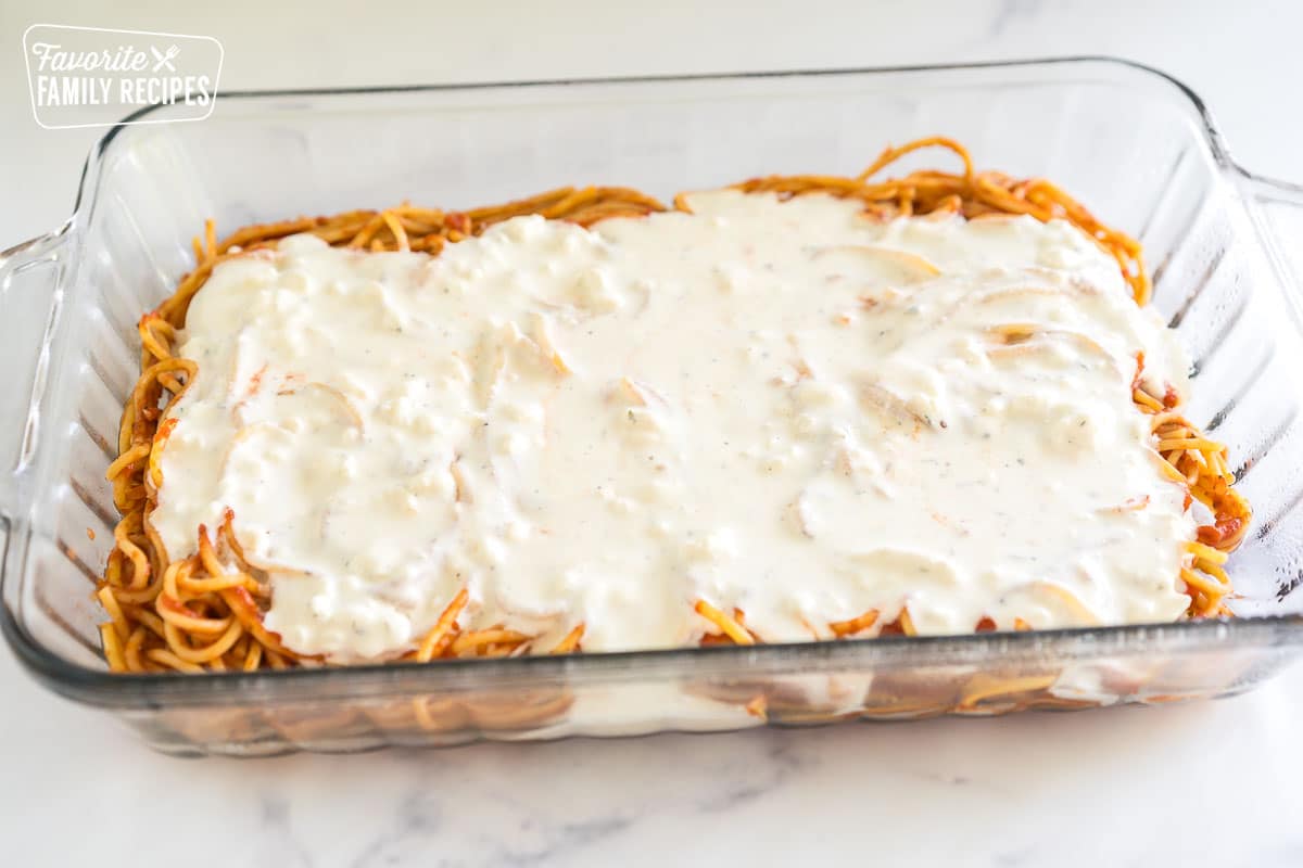 a baking dish with a layer of pasta with red sauce and a layer of cheese sauce