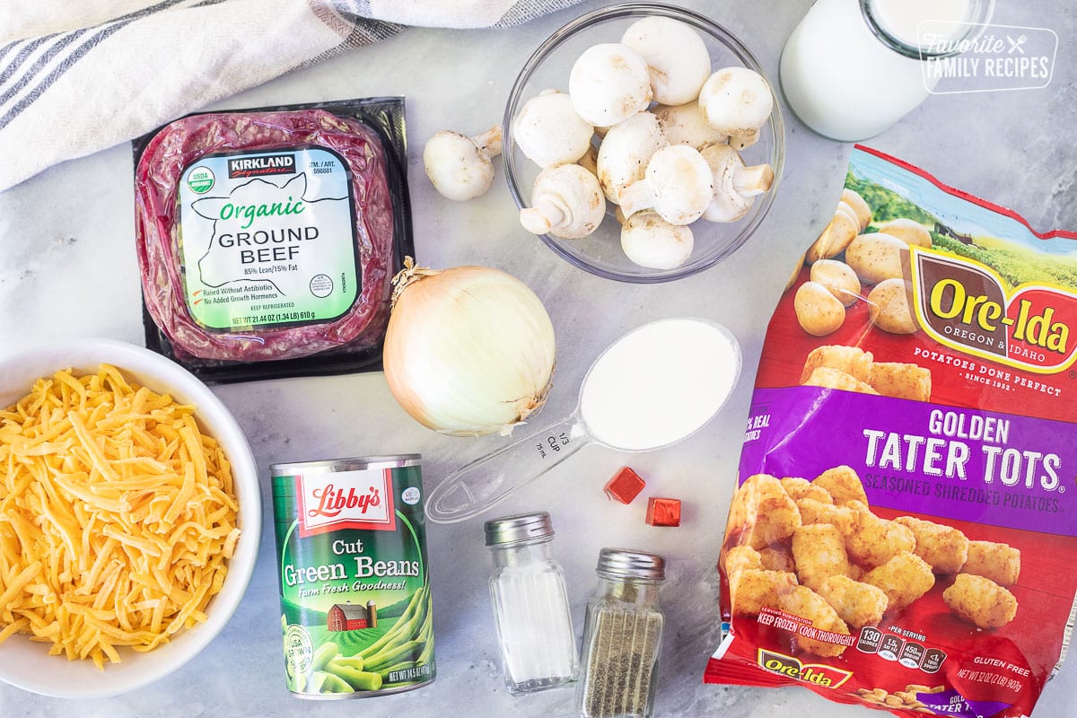 Ingredients for Tater Tot Casserole including ground beef, mushrooms, flour, onion, beef bouillon, milk, salt, pepper, tater tots, green beans and cheddar cheese.