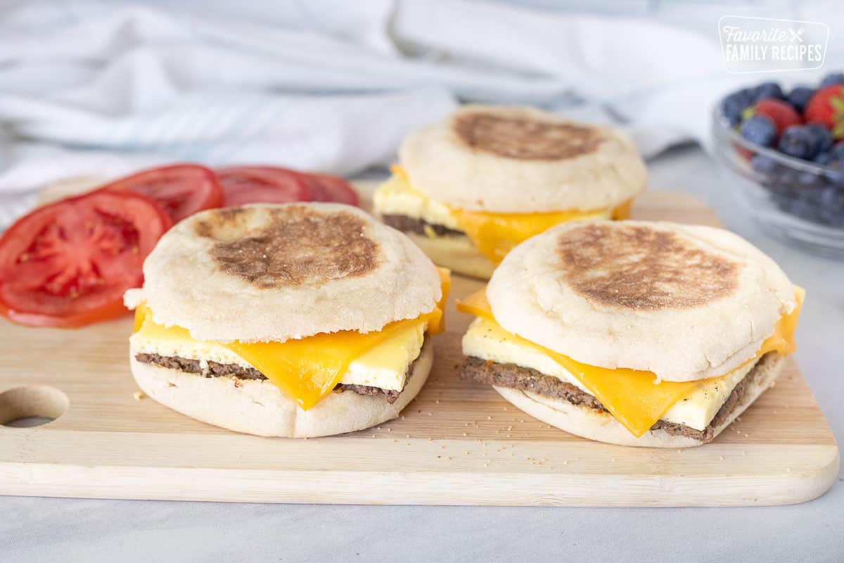 Cutting board with three heated Freezer Breakfast Sandwiches. Sliced tomato on the side.