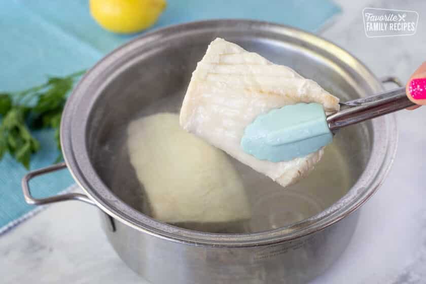 Tongs grabbing out cooked halibut from pan of water for Poor Man's Lobster.